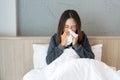 Sickness Asian woman sneezing into a tissue in bed room after wake up. Female illness from colds or flu. Allergy or health problem Royalty Free Stock Photo