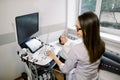 Side angle view of young woman doctor in white coat conducting ultrasound examination of abdomen to a female patient. Royalty Free Stock Photo