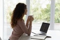 Dreamy young woman drinking coffee, distracted from computer work. Royalty Free Stock Photo