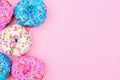 Side border of assorted donuts with pastel icing against a pink background