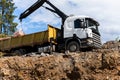 Side bottom pov big modern truck with mounted self loading crane arm boom unloading pallet of new bricks at countryside