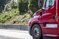 Side of the bright red big rig semi truck running on the road with forest on the hillside Royalty Free Stock Photo