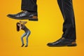 Side close-up of man`s feet in shoes, one foot in air ready to step on miniature young girl who`s covering her head in Royalty Free Stock Photo