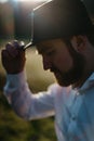 Side close-up outdoor portrait of the stylish handsome man with beard touching his black hat and looking down in the Royalty Free Stock Photo