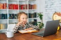 Side close-up view of serious Caucasian school girl doing homework sitting at table with laptop and paper notebook at Royalty Free Stock Photo