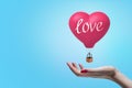 Side close-up of woman`s hand facing up to catch little heart-shaped hot-air balloon with title `love` on it. Royalty Free Stock Photo