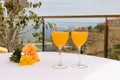 Side closeup of two glasses of orange juice on the white table outdoors, a yellow hibiscus rosa near Royalty Free Stock Photo