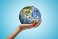 Side closeup of woman`s hand facing up and holding small Earth on light blue background.