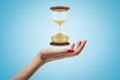 Side closeup of woman`s hand facing up and levitating hourglass on light blue background. Royalty Free Stock Photo