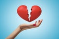 Side closeup of woman`s hand facing up and levitating red broken heart on light blue gradient background. Royalty Free Stock Photo