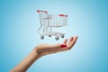 Side closeup of woman`s hand facing up and levitating small supermarket trolley on light blue gradient background. Royalty Free Stock Photo