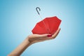 Side closeup of woman`s hand holding small red umbrella upside down on her palm on light blue gradient background. Royalty Free Stock Photo