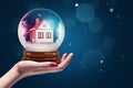 Side crop close-up of female`s hand facing up holding crystal ball with house inside. Royalty Free Stock Photo