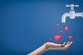 Side crop close-up of woman`s hand facing up and catching cute red hearts coming from grey tap on blue background with a