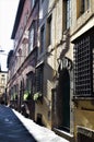 Side exposed to the inclined sun, of a street in the center of Lucca, with a door in the foreground and solid iron grates, on the