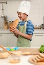Side of face kid eating large loaves of bread, happy Asian boy with apron and chef hat holding and eating freshly baked homemade Royalty Free Stock Photo
