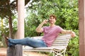 Side of laughing man sitting on park bench with suitcase and cellphone Royalty Free Stock Photo