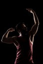 Side lit muscular Caucasian man silhouette. Athlete in red shirt posing against black background