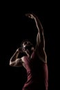 Side lit muscular Caucasian man silhouette. Athlete in red shirt posing against black background