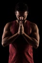 Side lit muscular Caucasian man silhouette. Athlete in red shirt praying against black background