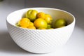 Side lit small and regular size yellow plums in white bowl