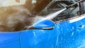 Side mirror of blue car washed in self serve carwash, jet water sprays from high pressure nozzle