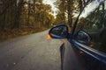 Side mirror turn signal. Turn indicator on the mirror left and blue car on the road in autumn forest. Car stands on the edge of