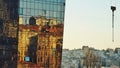 Side of a modern glass building with a crooked reflection of the city on the glass and a crane part