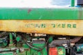 Side of an old, worn down classic tractor, showing remnants of the John Deere logo word mark in green and yellow, and tractor Royalty Free Stock Photo