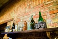 The side photo of the antique camera placed on the dark wooden shelf with colourful glass bottles hanging on the brick Royalty Free Stock Photo