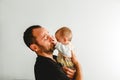 Side portrait of adorable baby in his father`s arms touching his face with his little hands, white background Royalty Free Stock Photo