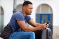 Side portrait of african man sitting outside with suitcase and using cell phone Royalty Free Stock Photo