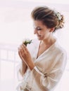 The side portrait of the bride in the silk robe holding the mini-bouquet consisted of white roses. Royalty Free Stock Photo