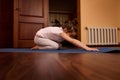 Lovely baby girl stretching her body in child pose, practicing yoga on a blue fitness mat in a cozy wooden home interior Royalty Free Stock Photo