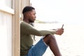 Side of handsome young black man sitting outdoors with cellphone Royalty Free Stock Photo
