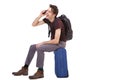 Side portrait of happy traveler talking on cellphone and sitting on suitcase