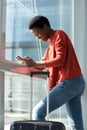 Happy young african american woman standing in airport terminal looking at cellphone by window Royalty Free Stock Photo