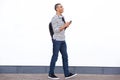 Side portrait of happy young man walking with bag and mobile phone against white wall Royalty Free Stock Photo