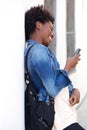 Smiling young woman leaning to wall and using cell phone Royalty Free Stock Photo