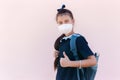 Side portrait of teenage girl with backpack and reusable thermo water bottle after school showing thumbs up. Wearing medical mask.
