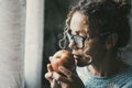 Side portrait of woman holding an apple and looking outside the window at home. Concept of healthy food lifestyle and fruit. Royalty Free Stock Photo