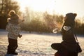 Young woman with little son throwing up snow on background of sunny winter park, photo against the sun. Happy family Royalty Free Stock Photo