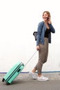 Side portrait of young travel woman walking and talking with mobile phone against white wall