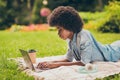 Side profile photo of black skinned young female student lying on grass using laptop focused on learning in the park Royalty Free Stock Photo