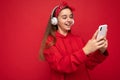 Side-profile photo of smiling Positive attractive brunette girl wearing red hoodie isolated on red background holding