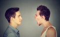 Side profile portrait of young angry man screaming at a calm smiling guy