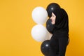 Side profile view Arabian muslim woman in hijab celebrating hold black white air balloons isolated on yellow background