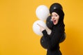 Side profile view Arabian muslim woman in hijab celebrating hold black white air balloons isolated on yellow background