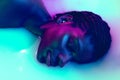 Profile view of female face of african girl in milk bath with soft white glowi in neon light. Modern neoned colors, foam