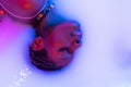 Profile view of female face of african girl in milk bath with soft white glowi in neon light. Modern neoned colors, foam